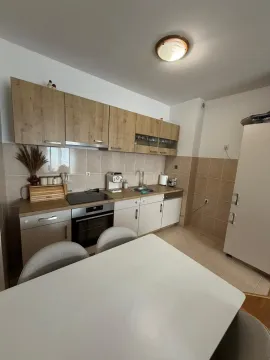 Kuhinja sa drvenim elementima i bijelim radnim površinama, sa trpezarijskim stolom u prvom planu. - image 6