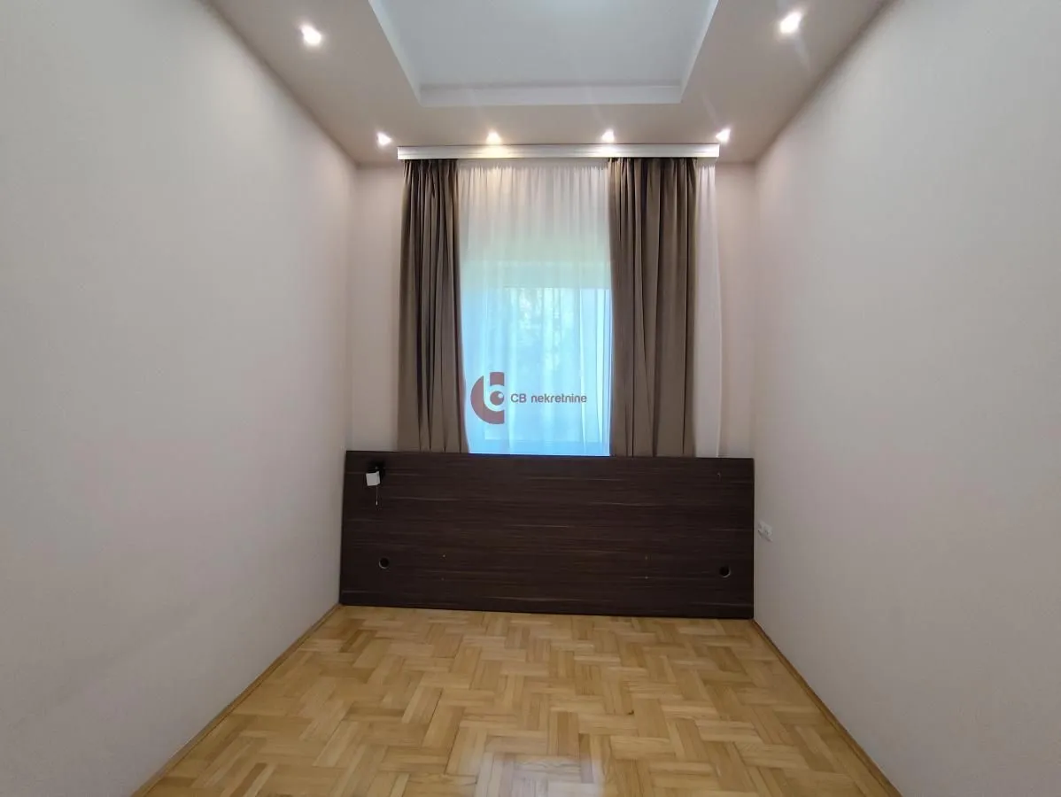 Empty bedroom with parquet flooring and a window with curtains.