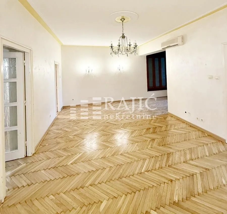 Empty living room with wooden parquet flooring and a chandelier.