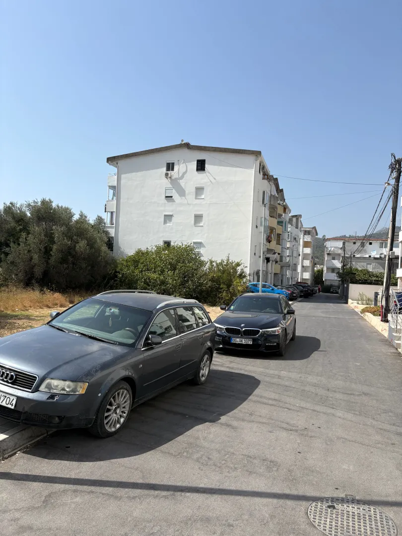Pogled na stambenu zgradu i ulicu sa parkiranim automobilima.