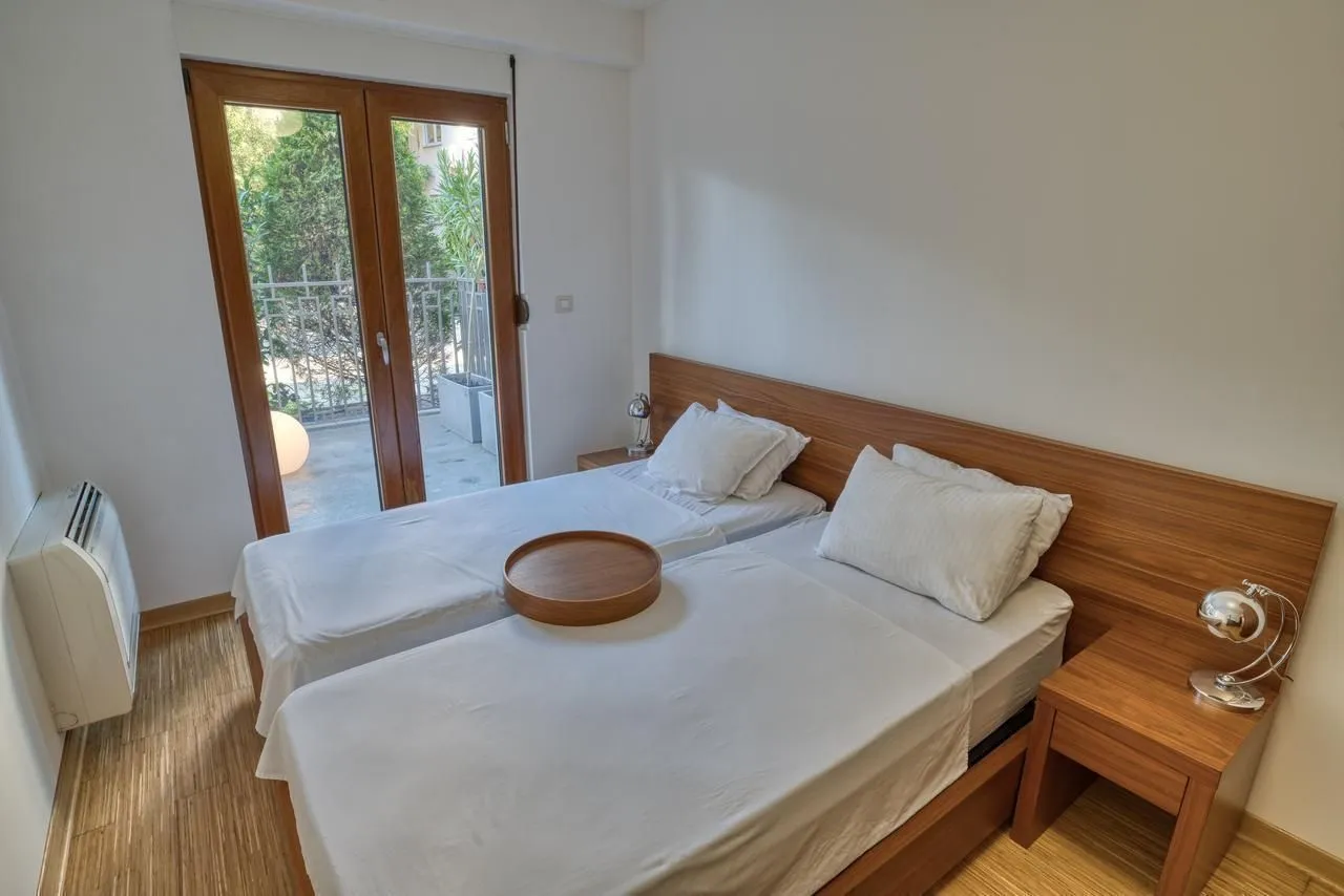 Svijetla spavaća soba sa dva singl kreveta i izlazom na balkon.