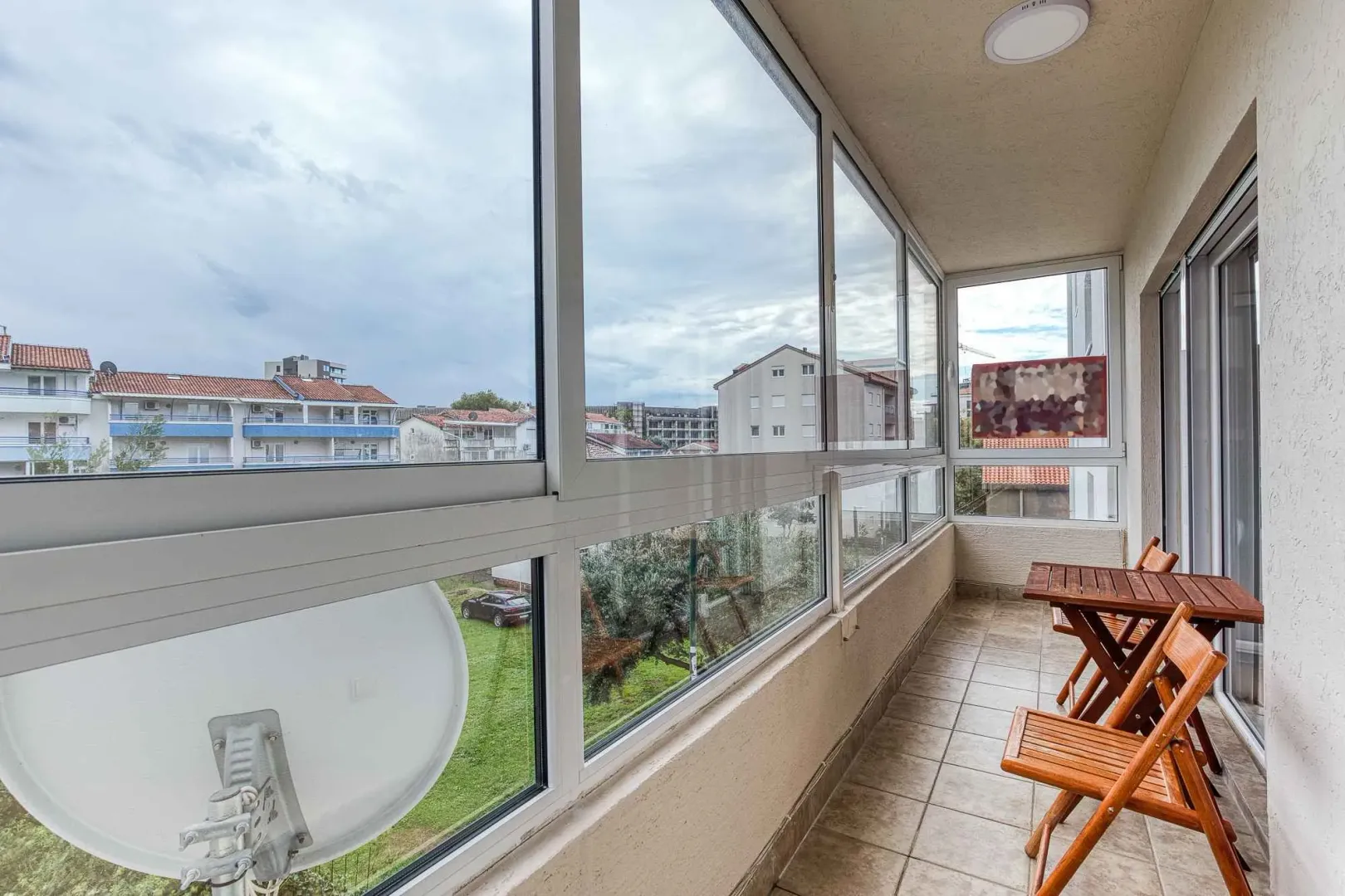 Enclosed balcony with a wooden table and chairs and a view of the neighborhood.