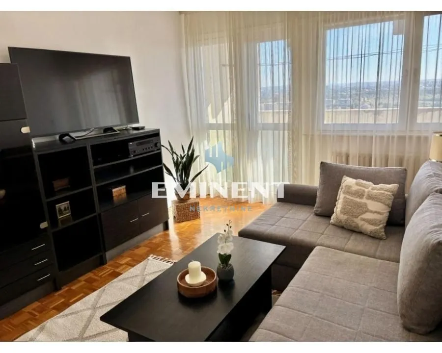 Furnished living room with a corner sofa, television and large windows.