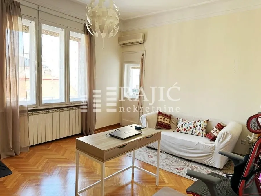 Living room with sofa, desk, and large windows.