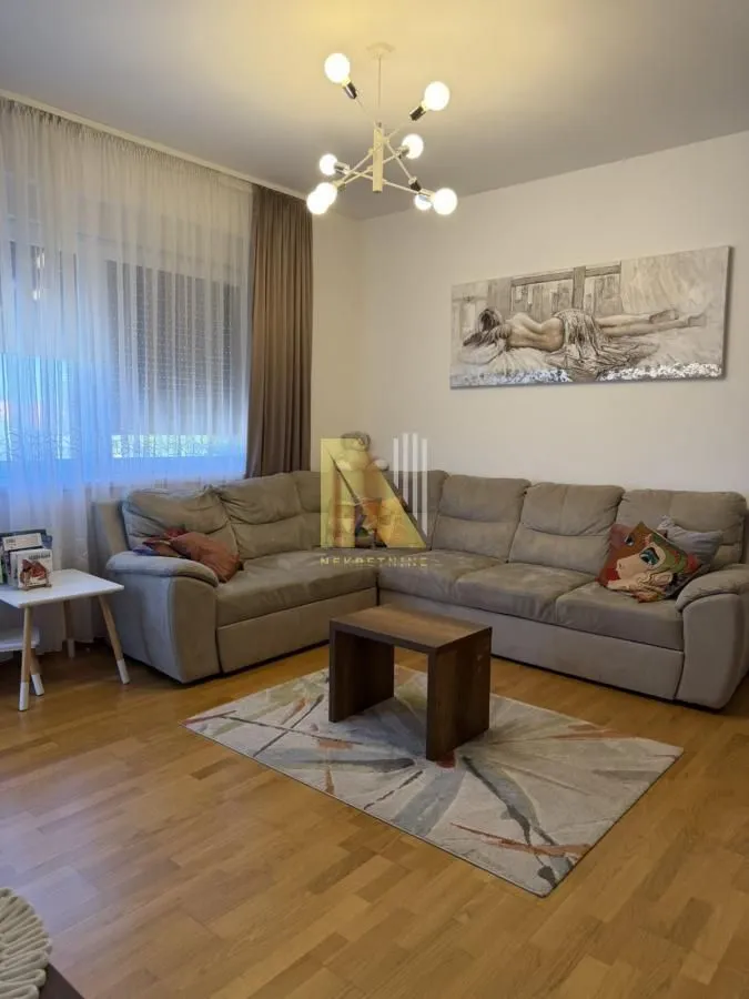 Dnevna soba sa ugaonom garniturom, stočićem i umetničkom slikom na zidu.