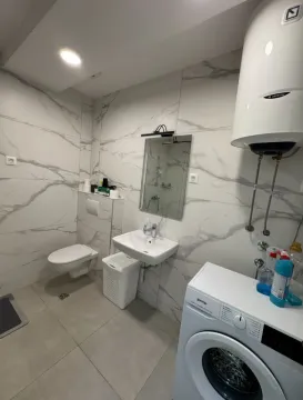 Bright bathroom with a washing machine, sink, and toilet. - image 5