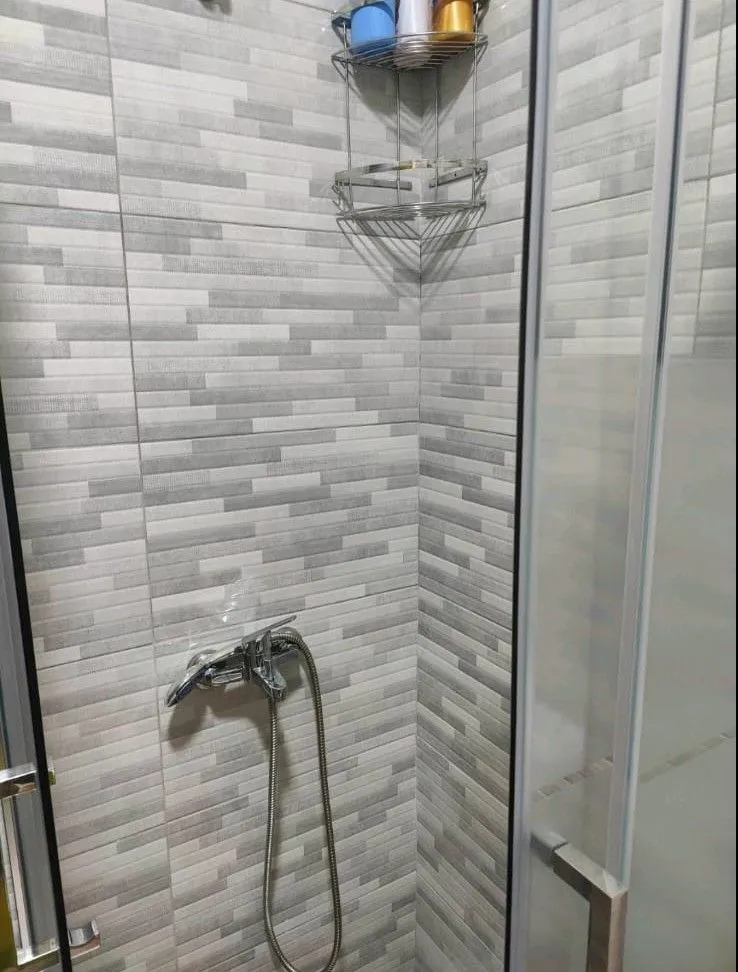 Modern shower cabin with grey tiles and chrome fixtures.