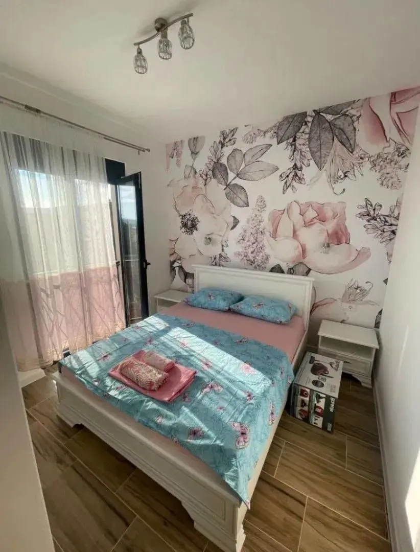 Spavaća soba sa bračnim krevetom, tapetama sa floralnim motivima i izlazom na terasu.
