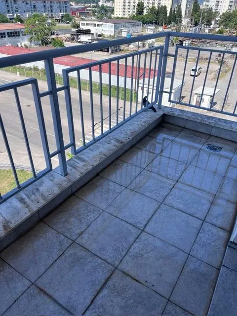 Manji popločani balkon sa metalnom ogradom i pogledom na okolinu.