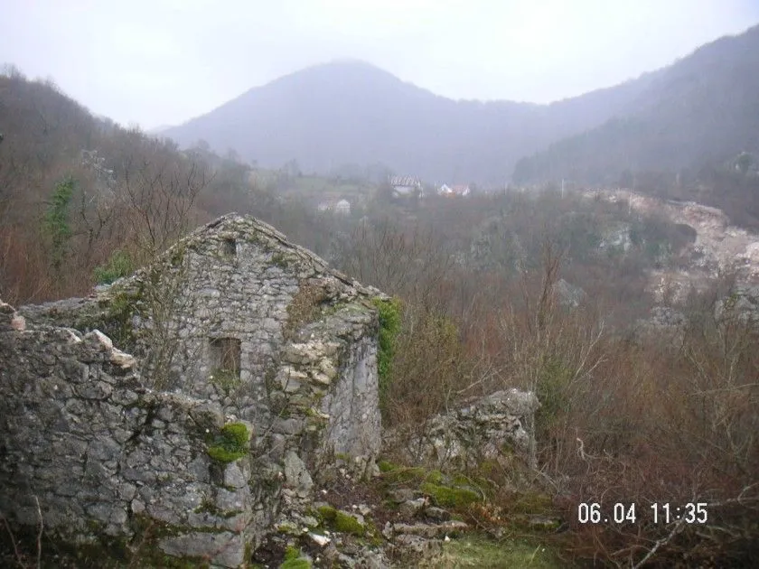 Ruševna kamena kuća u prirodnom okruženju sa pogledom na brda.