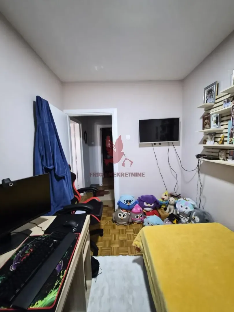 Dečja soba sa krevetom, radnim stolom i televizorom na zidu.