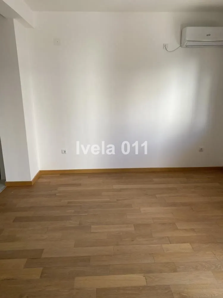 Prazna soba sa drvenim podom i klima uređajem na zidu.