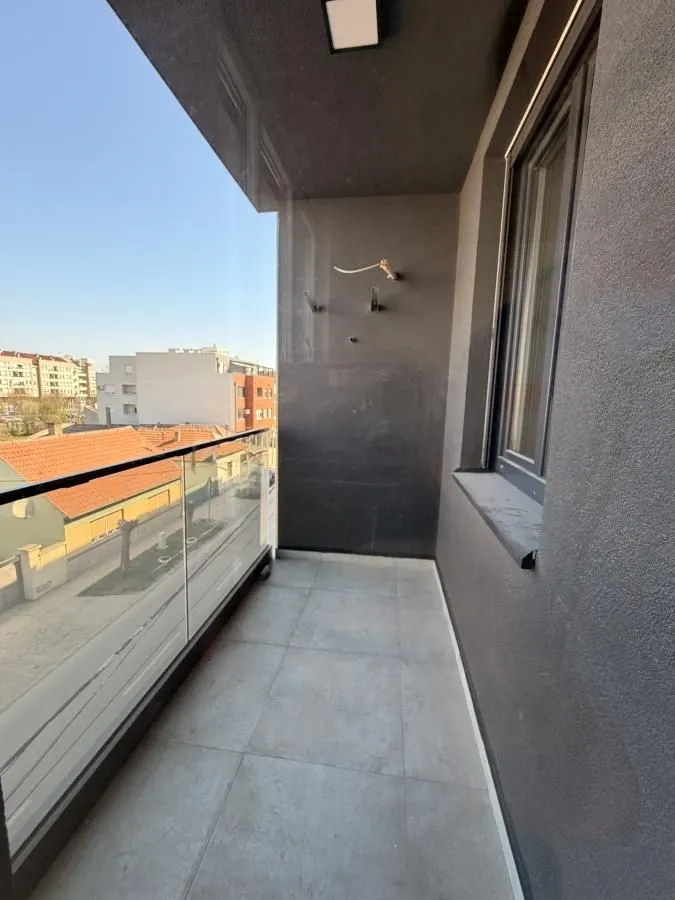 Nenameštena terasa sa staklenom ogradom i pogledom na okolne zgrade i ulicu.