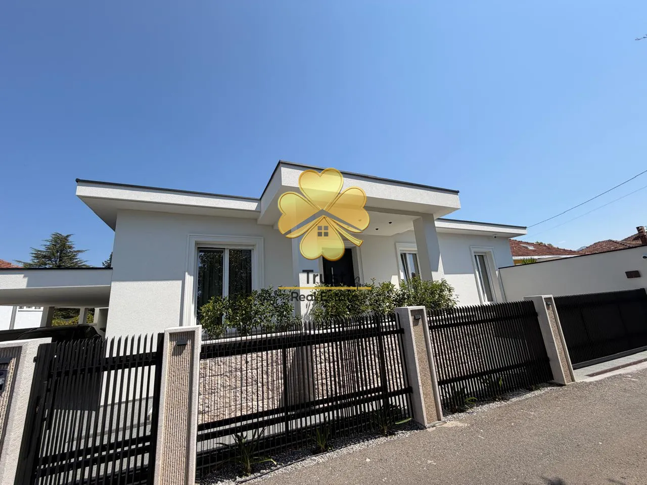 Eksterijer moderne kuće sa dvorištem i ogradom.