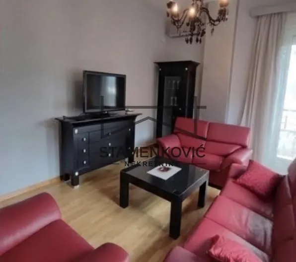 Dnevna soba sa crvenim garniturama za sedenje, TV komodom i lusterom.
