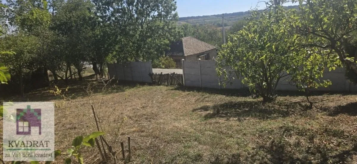 Pogled na dvorište i okolno zelenilo sa ogradom.