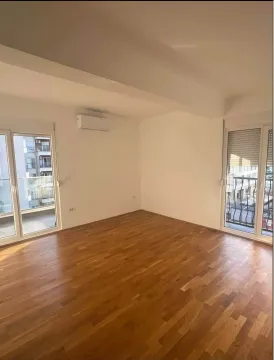 Empty room with hardwood flooring, white walls, and two balcony doors. - image 2