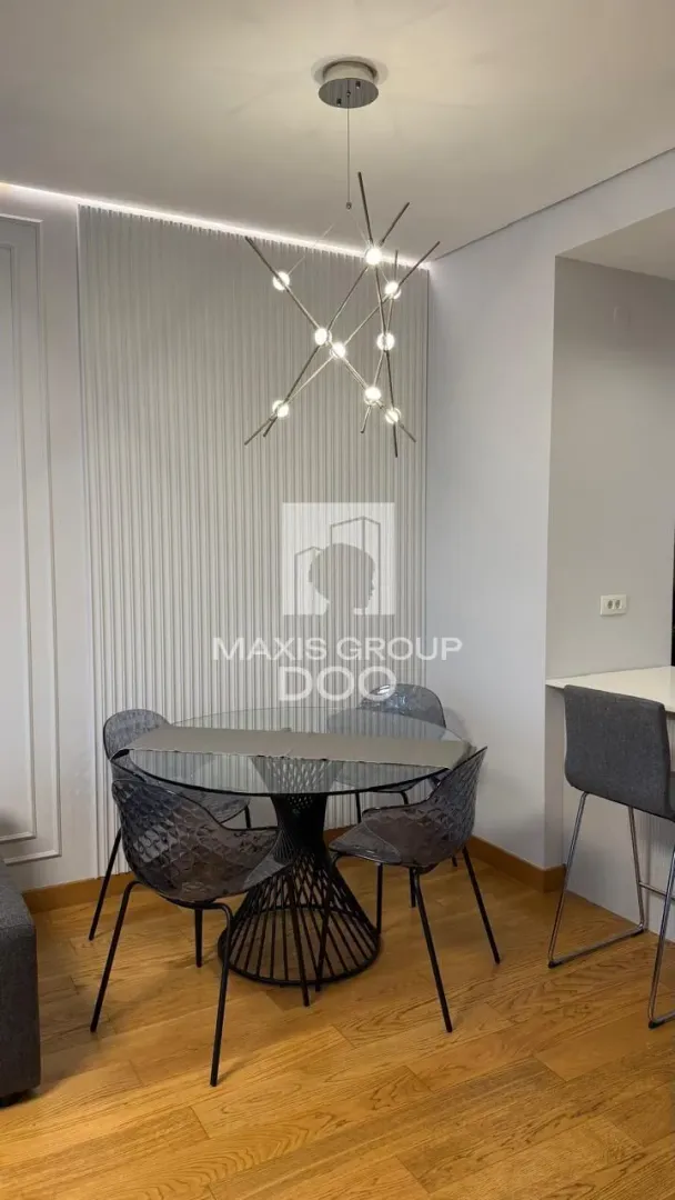 Dining area with a round glass table and modern chairs beneath a unique chandelier.