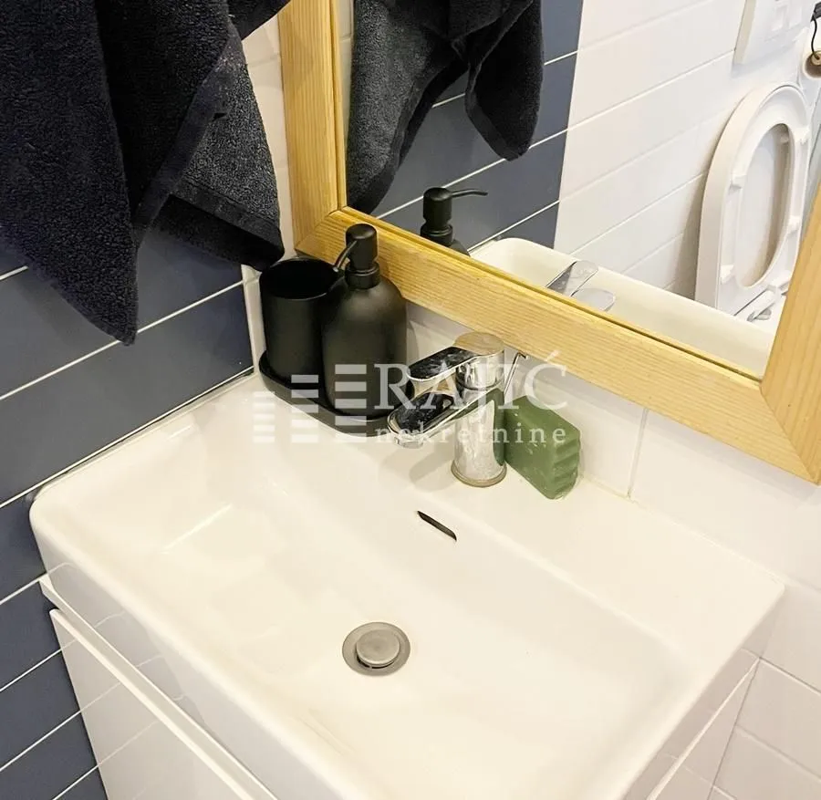 Modern bathroom with a white washbasin and a wooden-framed mirror.