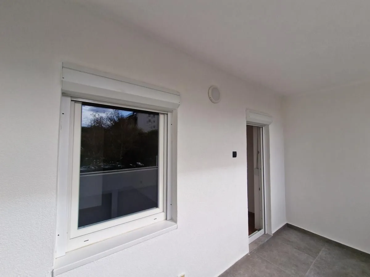 Natkriveni balkon sa prozorom i vratima na belom zidu.