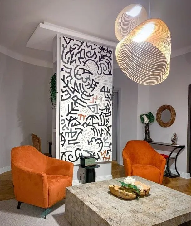 Moderan dnevni boravak sa narandžastim foteljama, ukrasnim panoom i modernim lusterom.