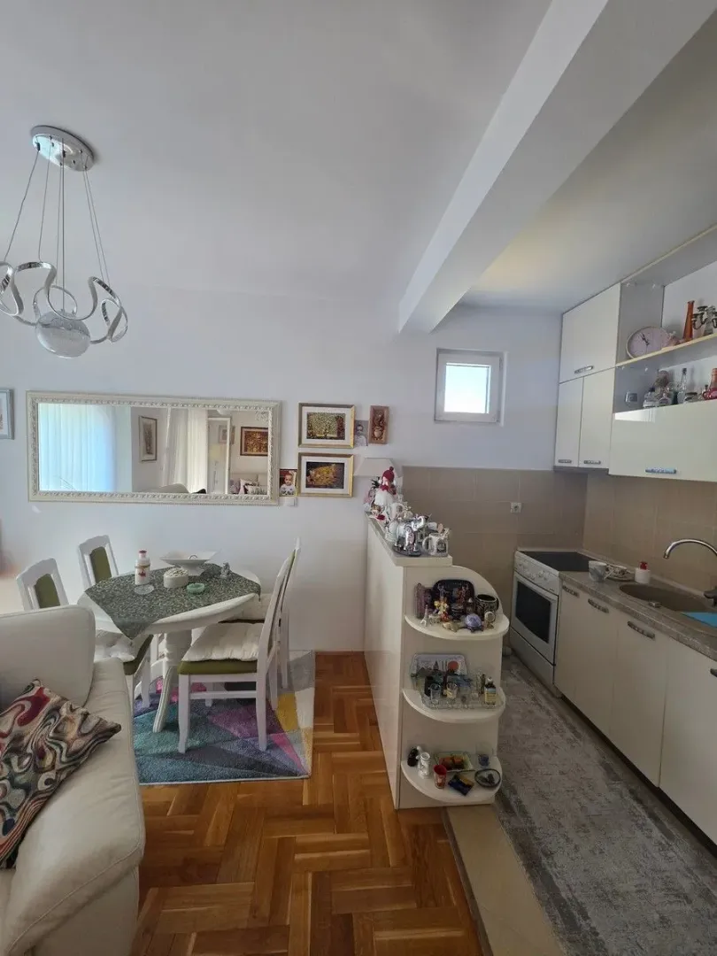 Otvoreni prostor kuhinje i trpezarije sa bijelim elementima i trpezarijskim stolom.