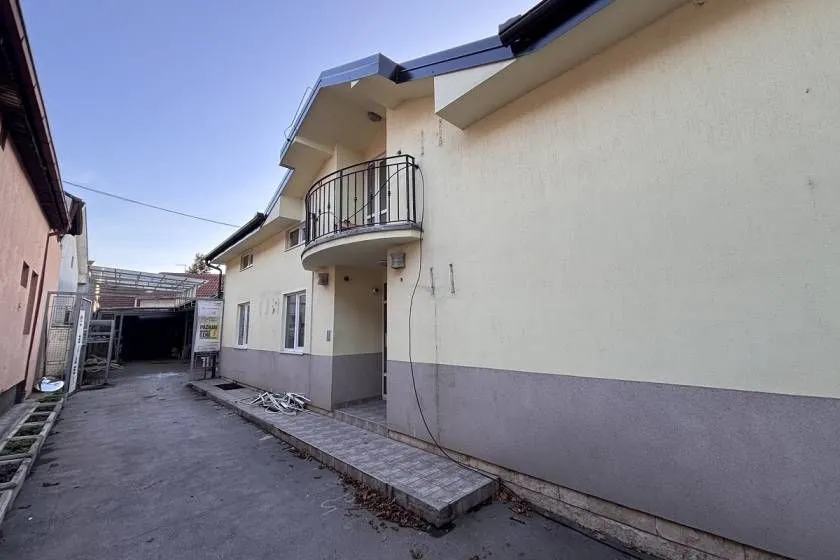 View of the exterior of the house with a balcony and a paved walkway.