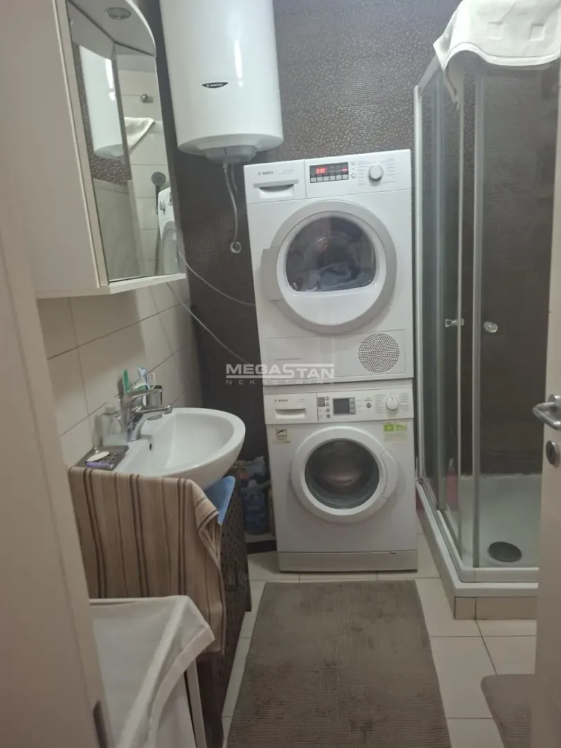 Bathroom with a shower cabin, washbasin, and a stacked washing machine and dryer.