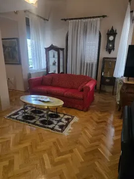 Spacious living room with a red sofa, wooden parquet flooring, and traditional furniture. - image 17