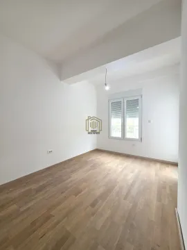 Prazna soba sa bijelim zidovima, drvenim podom i prozorom. - image 4