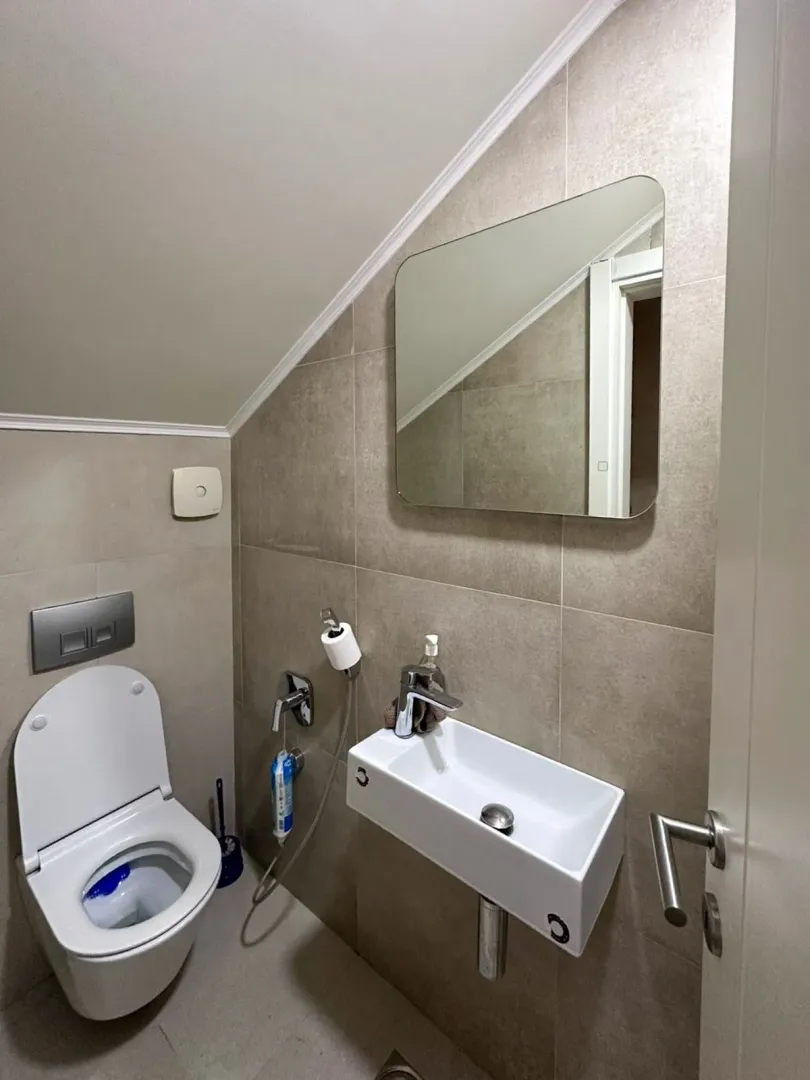 Manje kupatilo sa wc šoljom, umivaonikom i ogledalom.