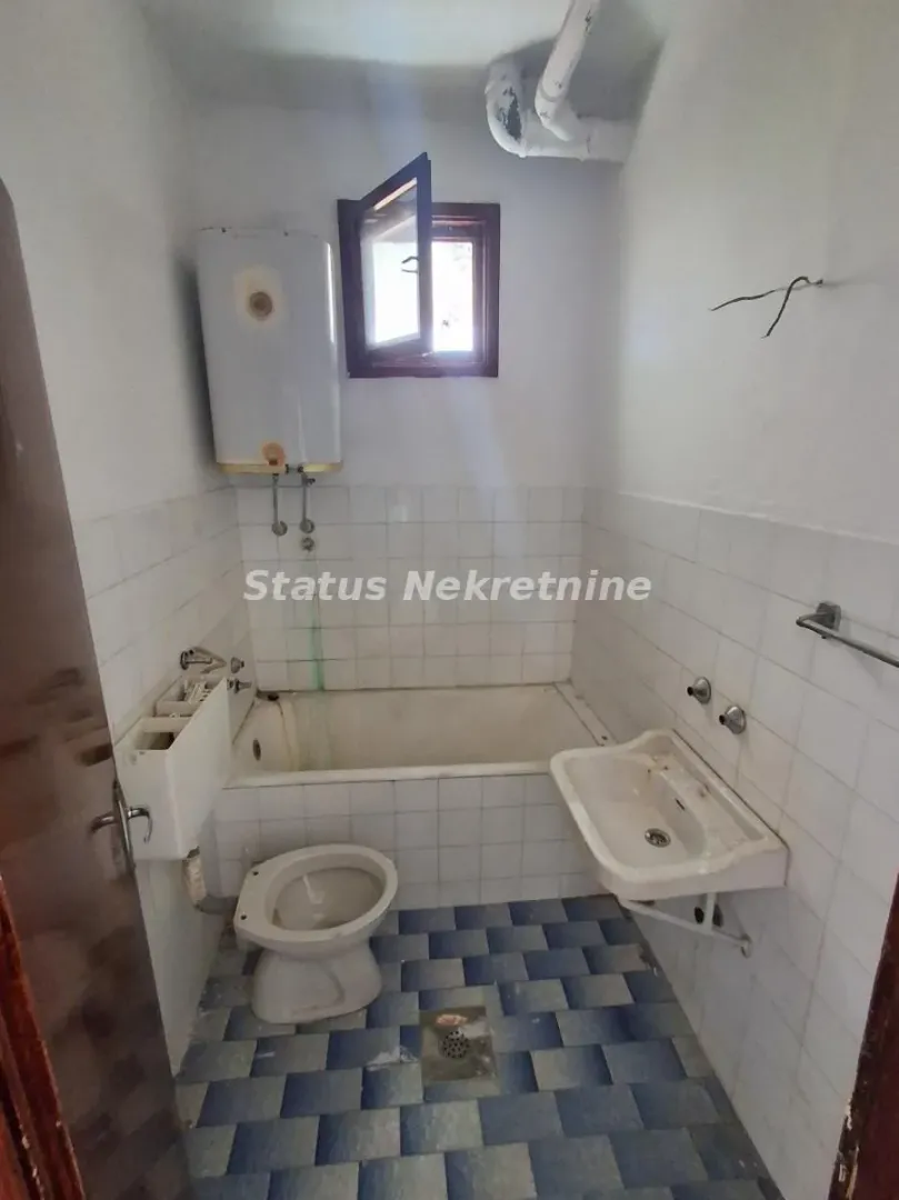 Starije kupatilo sa kadom, umivaonikom, WC šoljom i bojlerom.