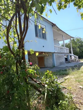 Pogled na dvorište i fasadu kuće sa balkonom i zelenilom u prvom planu. - image 16