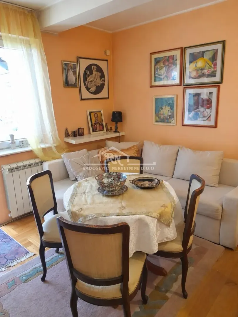 Living room with a corner sofa, dining table, and paintings on the wall.