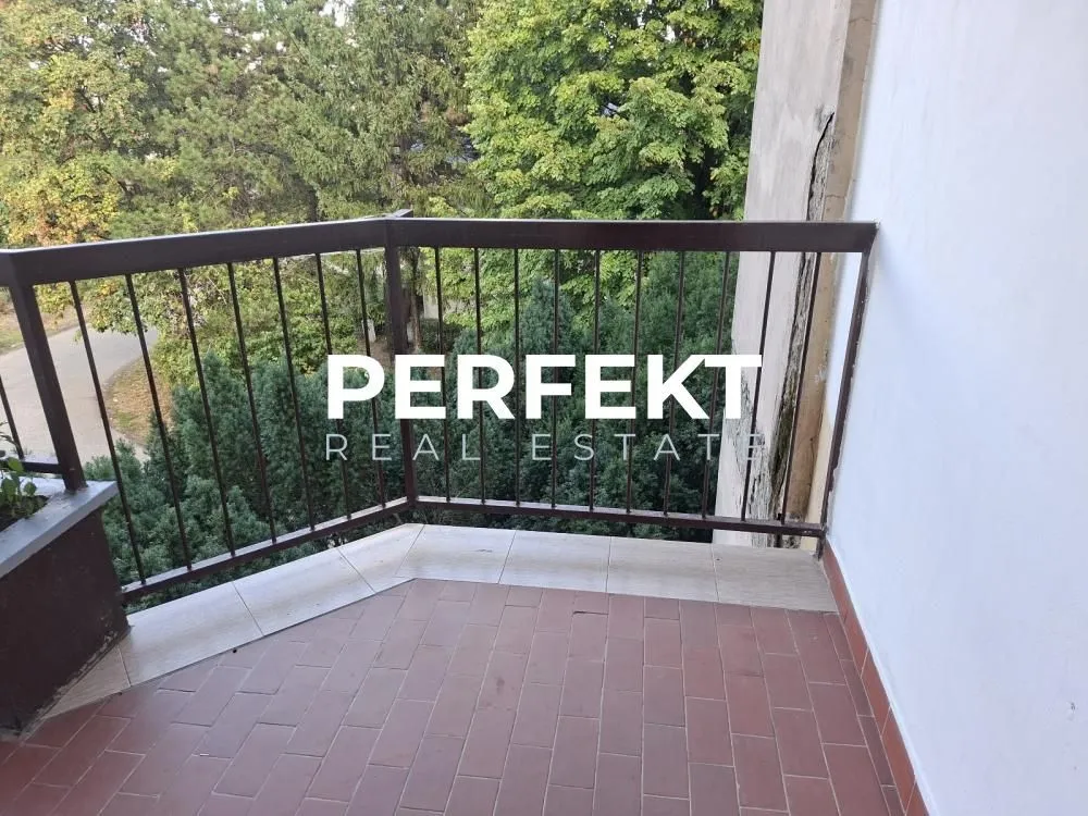 Balkon sa popločanim podom i metalnom ogradom sa pogledom na zelenilo.