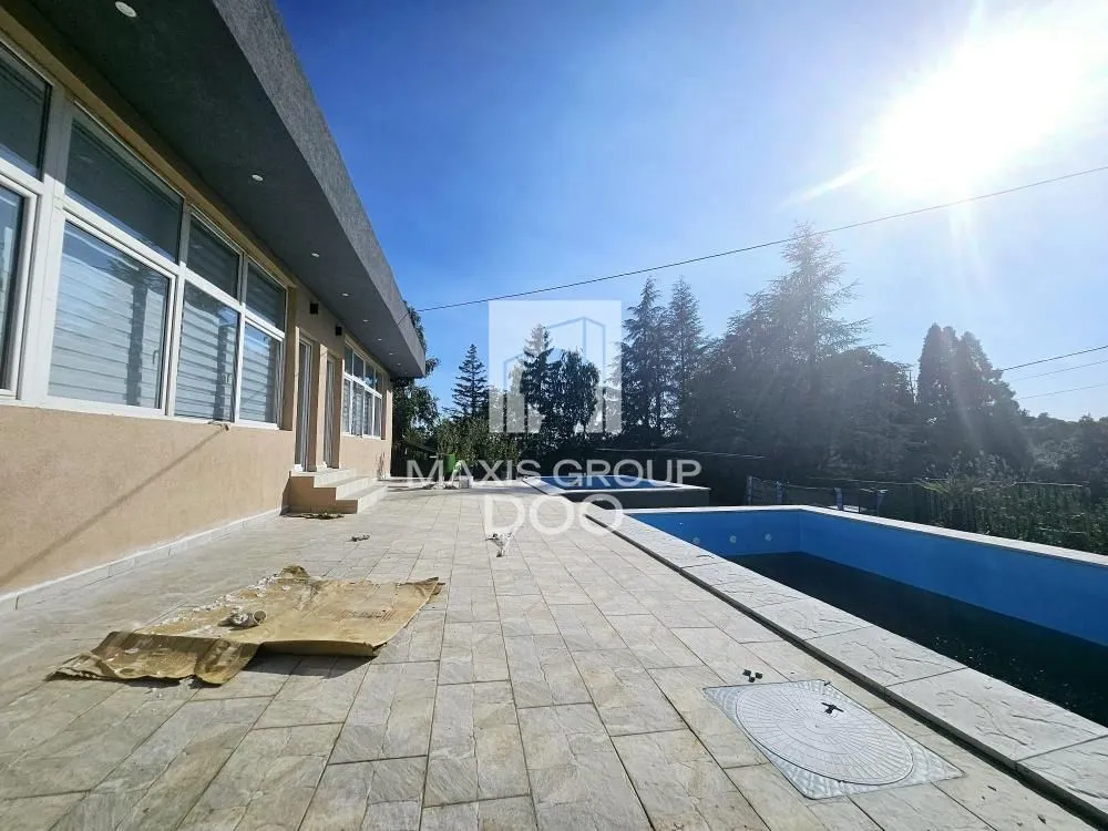 Dvorište sa popločanom terasom i bazenom ispred kuće.