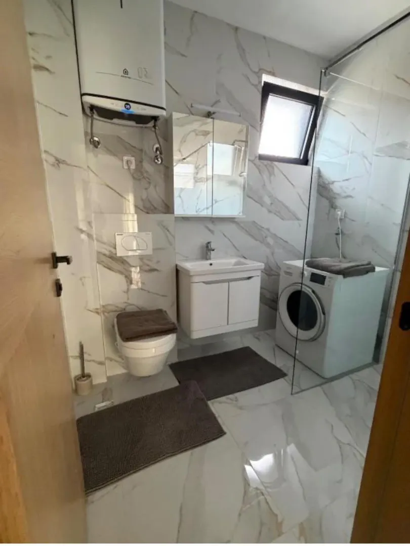 Moderne opremljeno kupatilo sa tuš kabinom, umivaonikom, WC šoljom i veš mašinom.