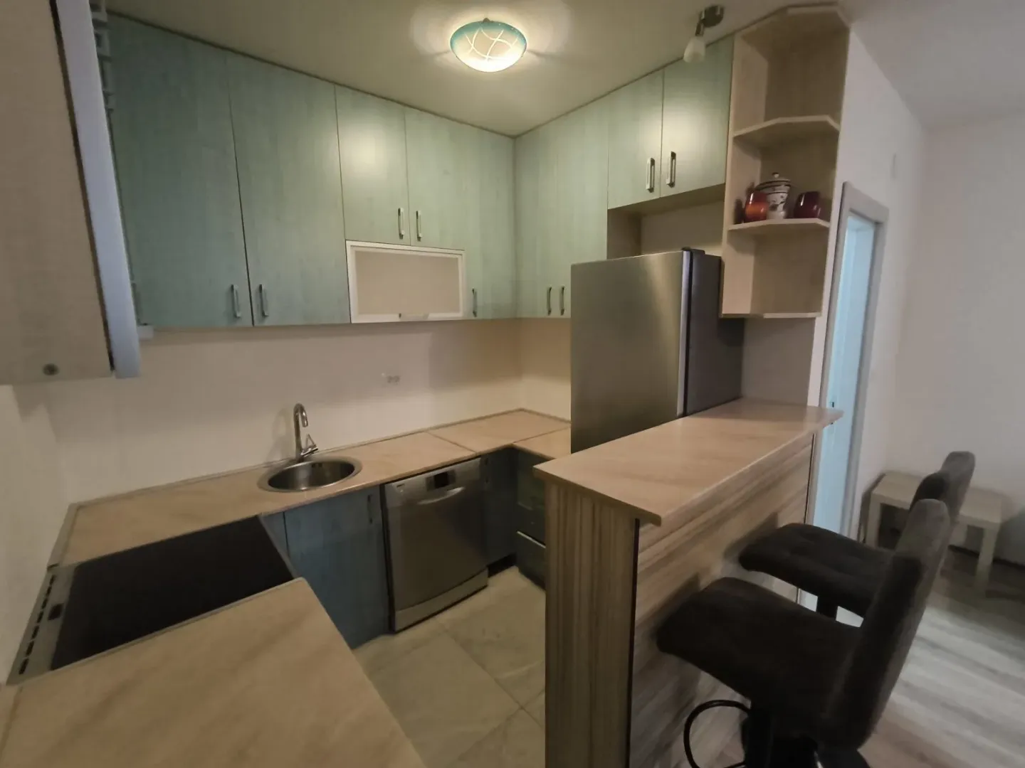 A kitchen with light blue cabinets, a bar counter, and bar stools.