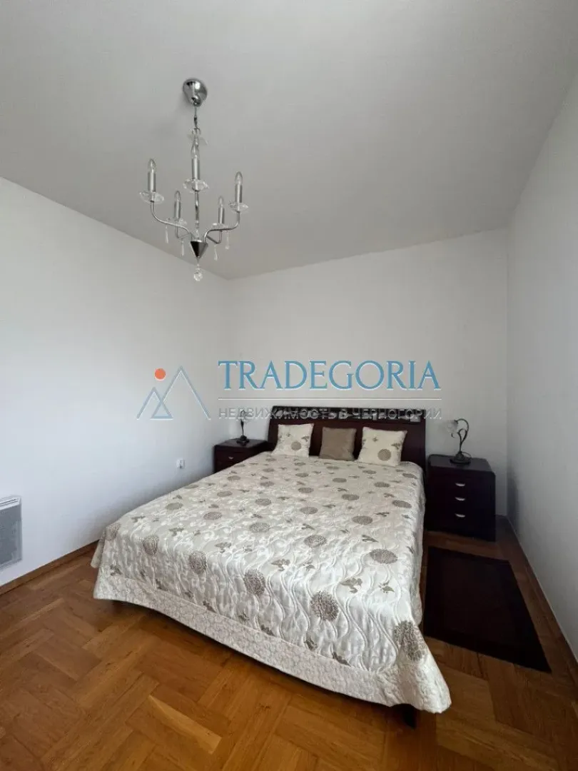 Spavaća soba sa bračnim krevetom, noćnim ormarićima i lusterom.
