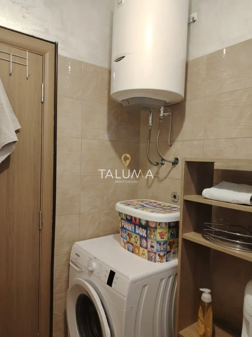 Bathroom with a washing machine, water heater, and a wooden shelf.