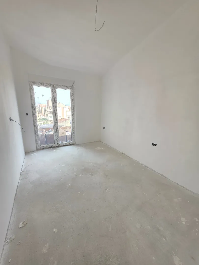 Prazna prostorija u izgradnji sa bijelim zidovima i balkonskim vratima.