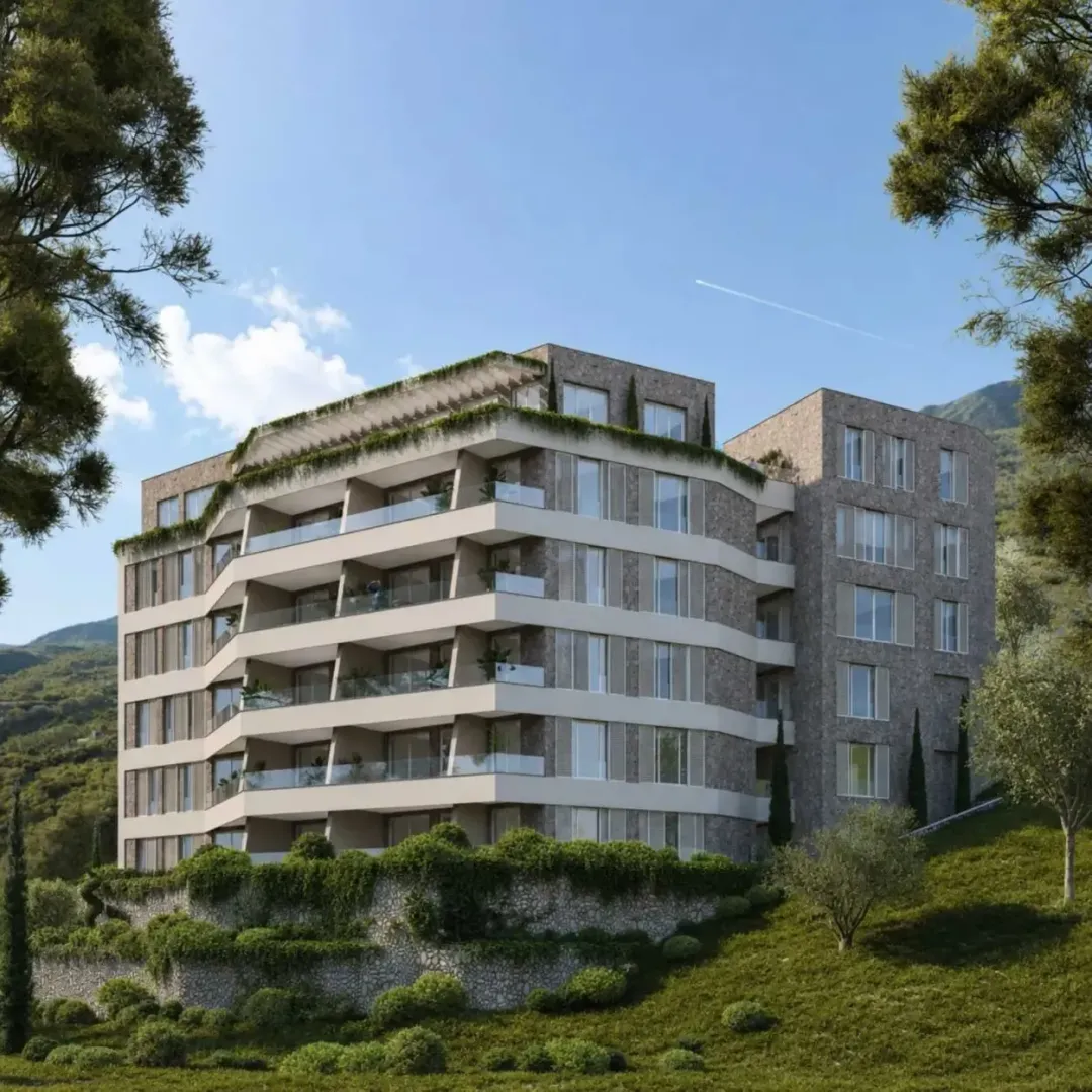 Spoljašnji izgled moderne stambene zgrade okružene zelenilom i planinskim pejzažom.