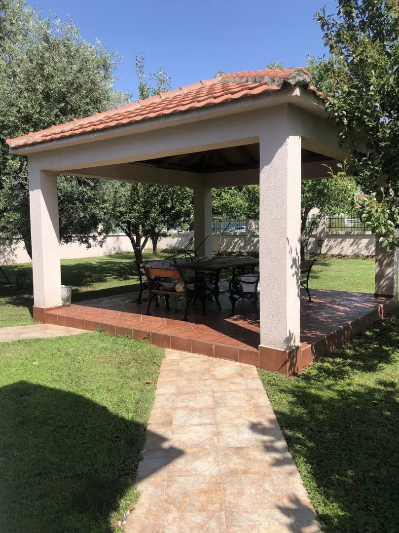 A covered gazebo in a spacious and landscaped yard with greenery.