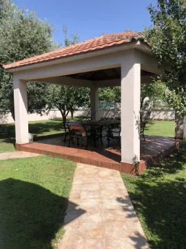 A covered gazebo in a spacious and landscaped yard with greenery. - image 6