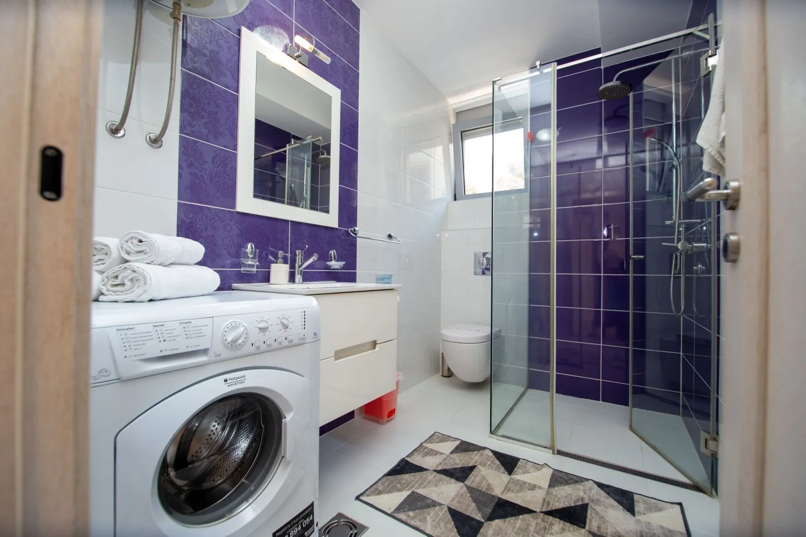 Modern bathroom with a walk-in shower, washbasin, and washing machine.