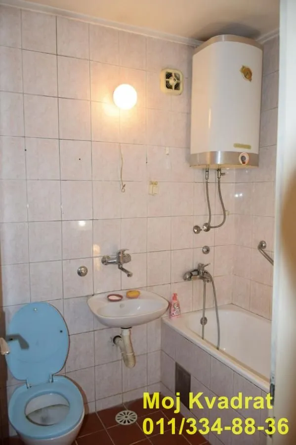 Manje kupatilo sa kadom, umivaonikom, WC šoljom i bojlerom na zidu.