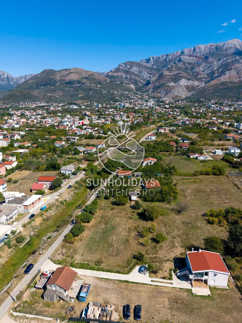 Pogled iz vazduha na okolinu i naselje sa planinama u pozadini.