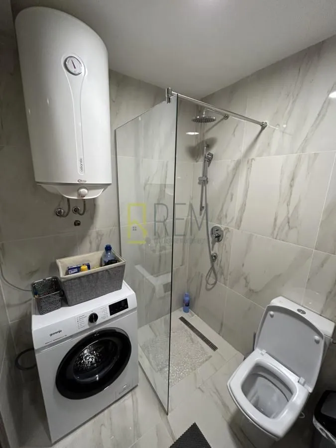 Modern bathroom equipped with a walk-in shower, washing machine, and water heater.