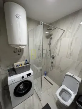 Modern bathroom equipped with a walk-in shower, washing machine, and water heater. - image 5