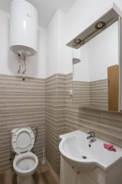 Smaller bathroom with brown-toned tiles, toilet, washbasin, and water heater. - image 7